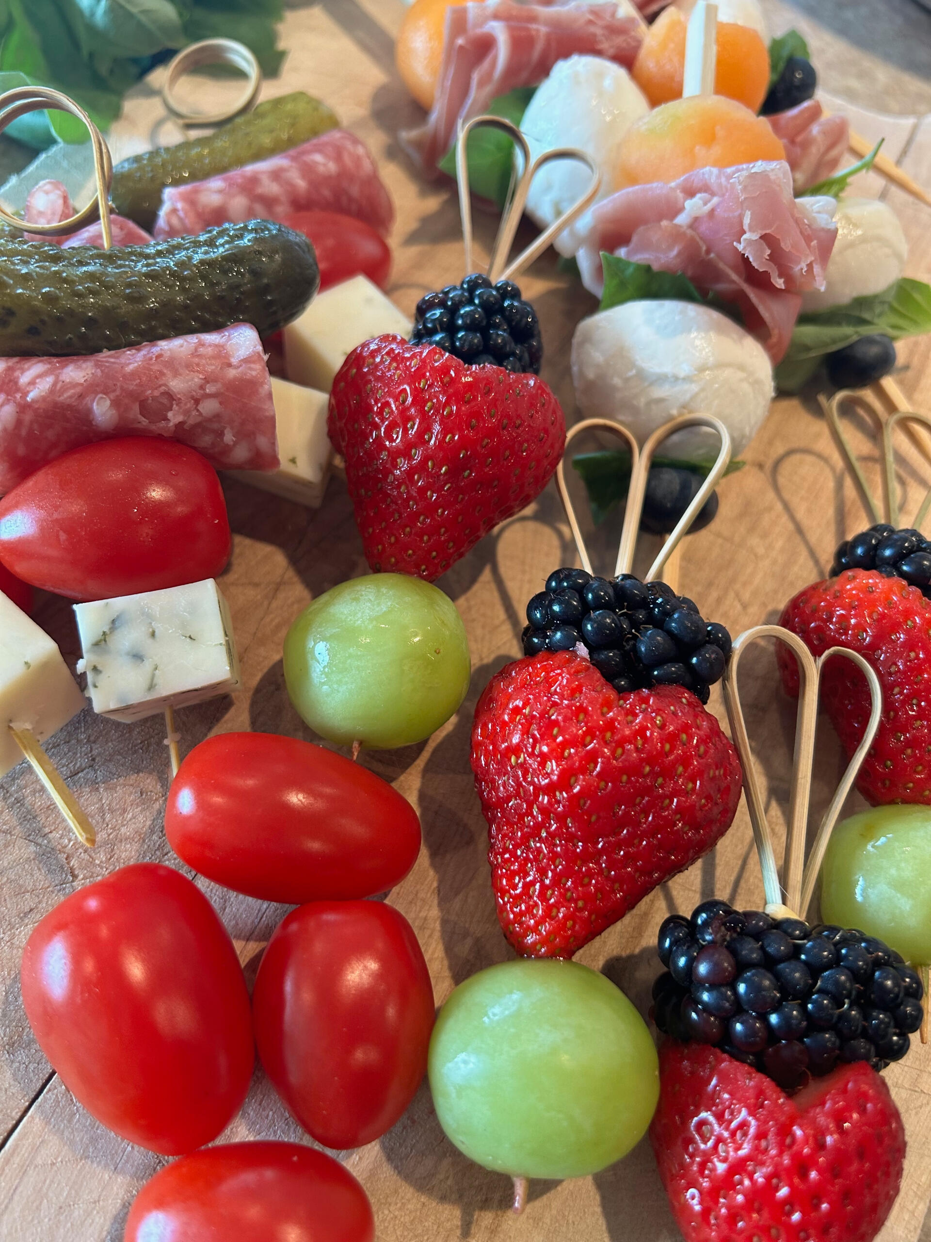 Skewers of strawberries, blackberries, pickles, cherry tomatoes, salami and prosciutto