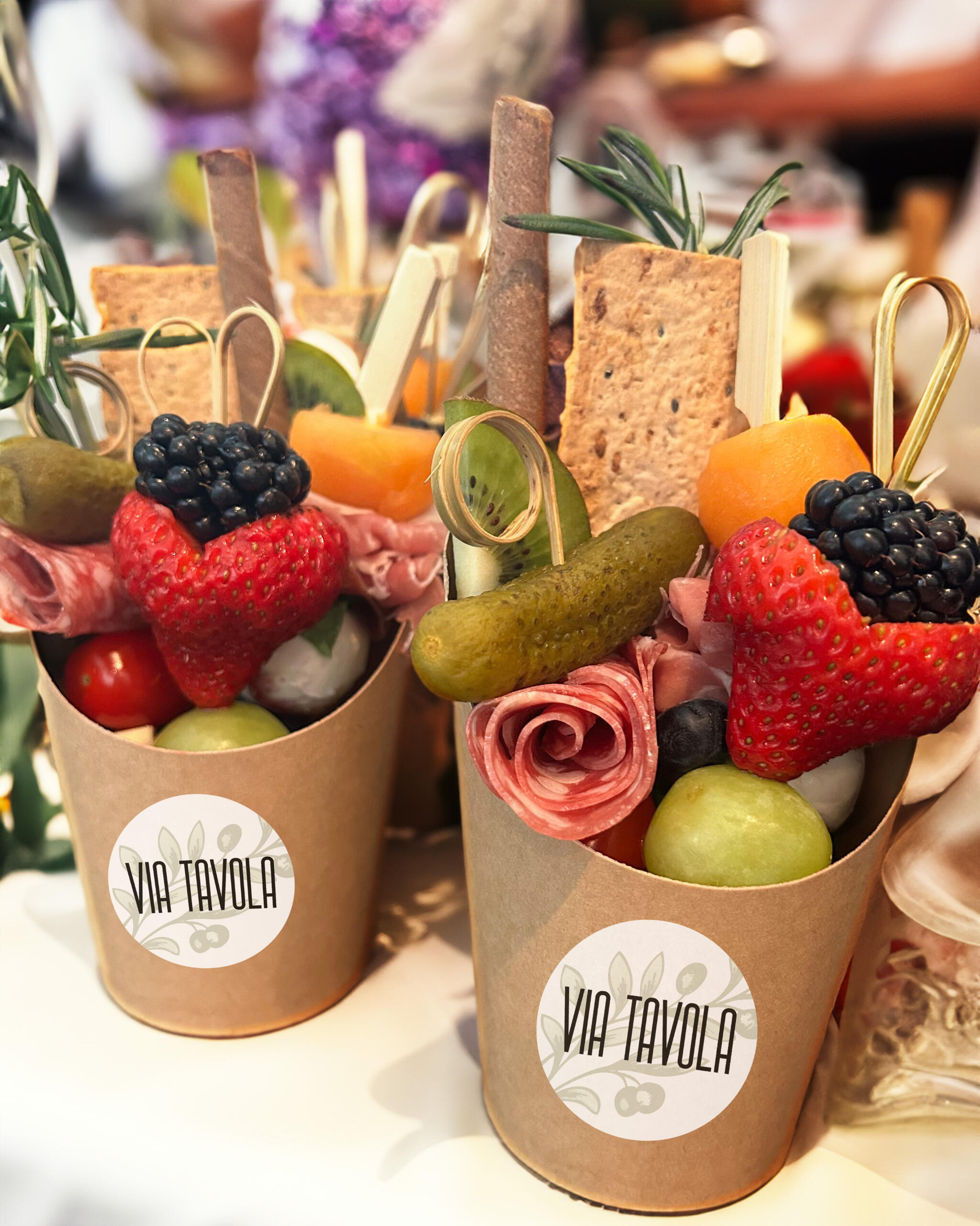 Charcuterie cups filled with crackers, skewers with fruit, meat skewers, and a pretty sprig of rosemary